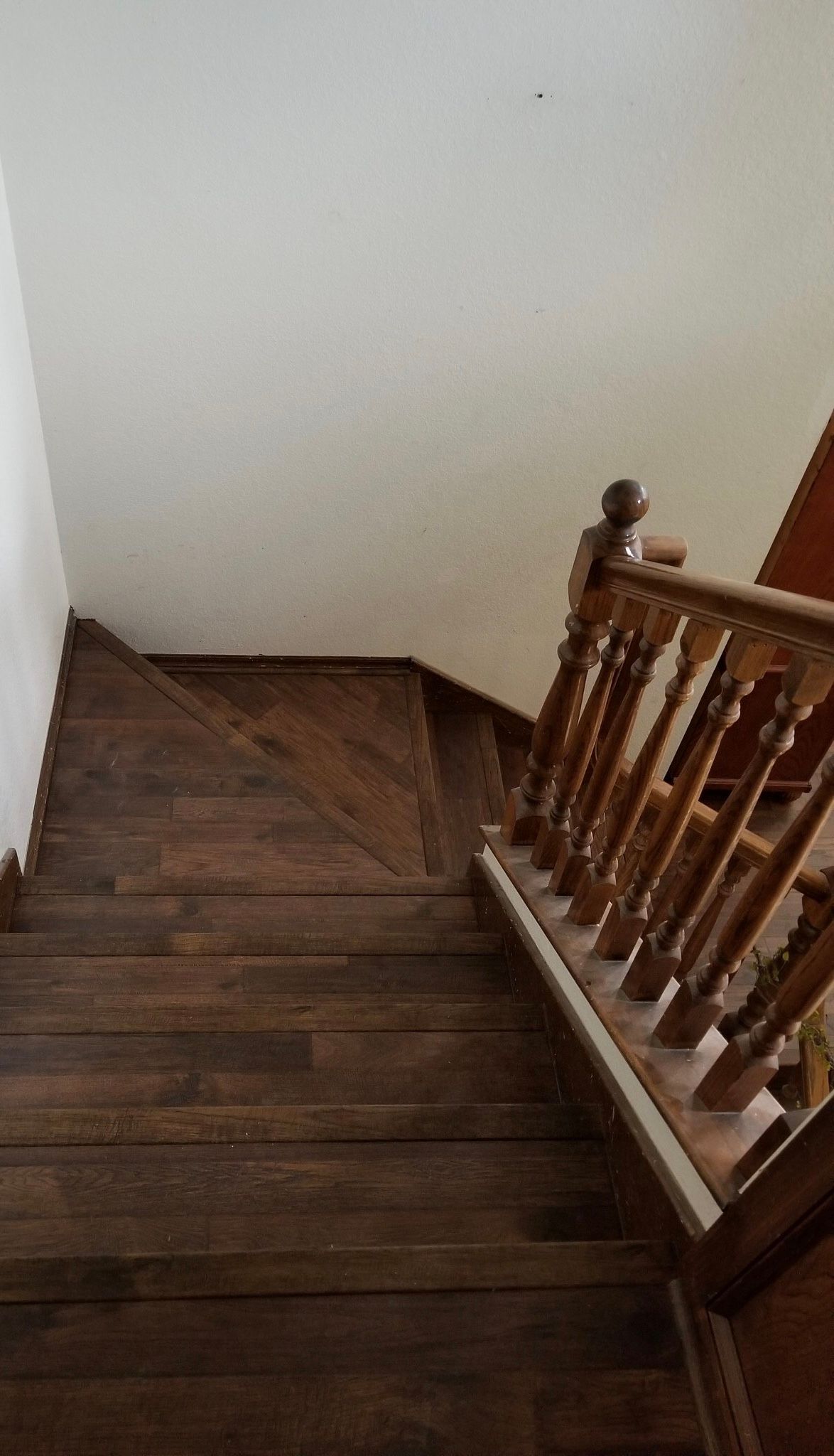 Wooden staircase descending to a landing, with a white wall and banister on the right.