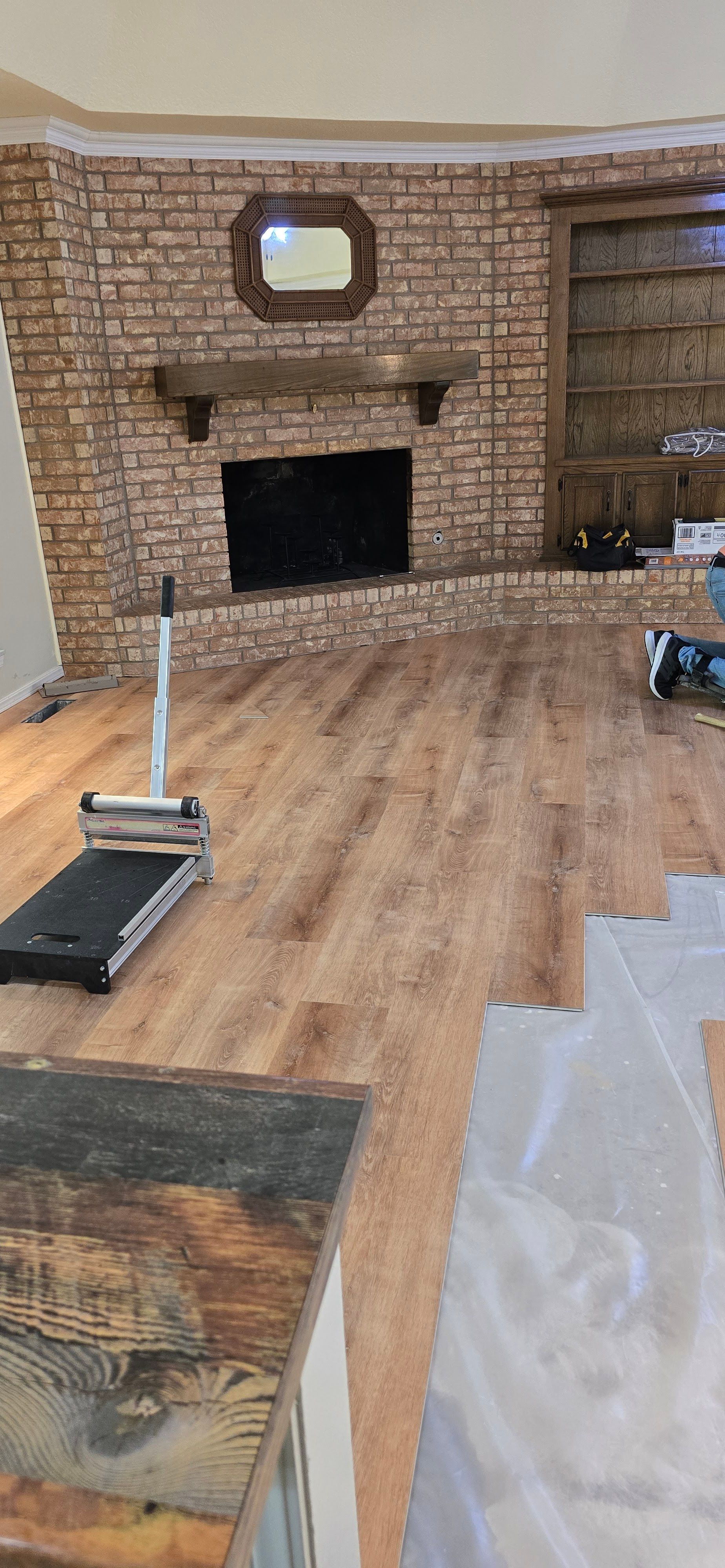 Empty living room with brick fireplace, wood floor, and protective plastic sheeting during renovation