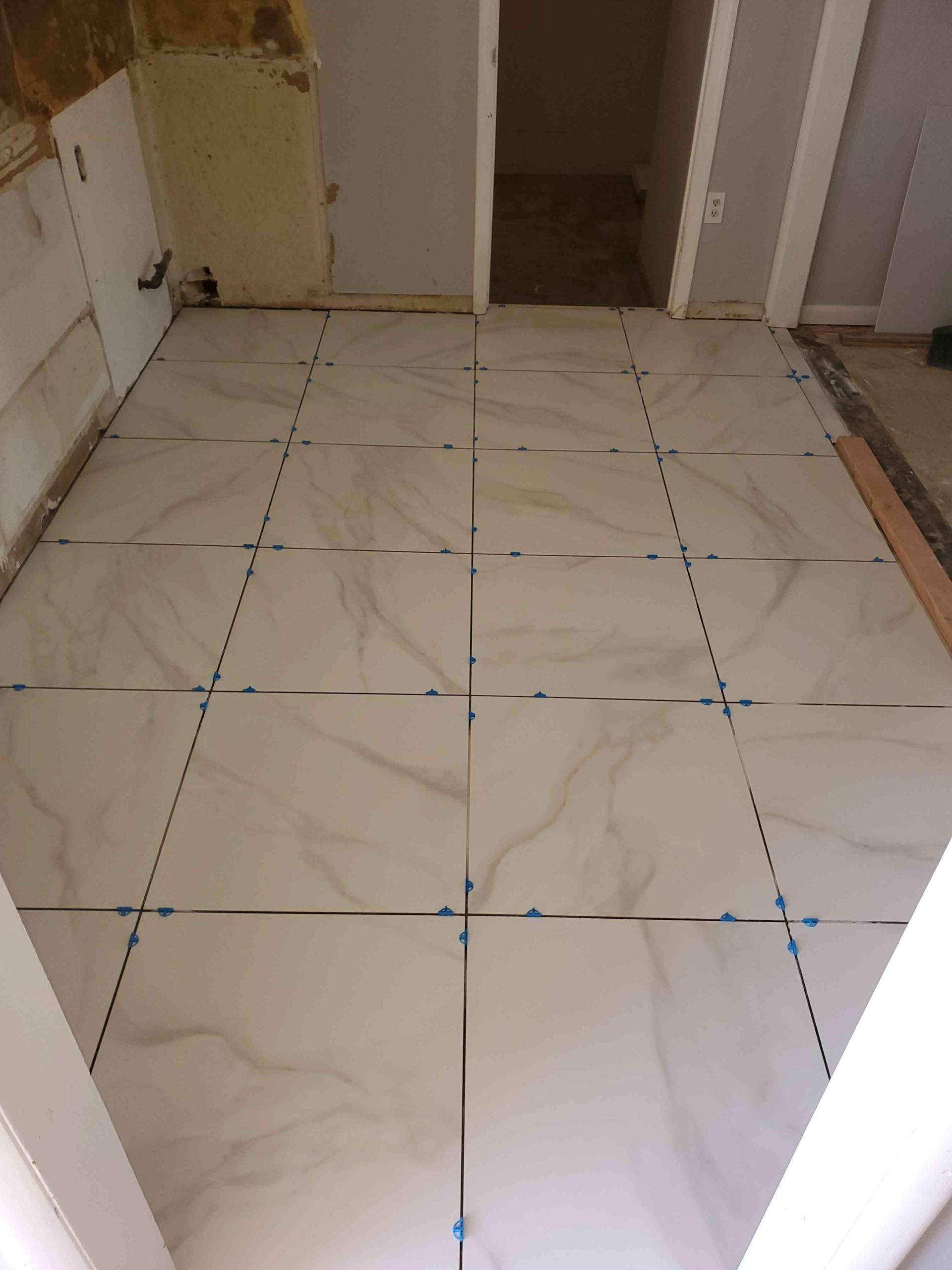 Empty room with a partially installed white tiled floor and blue alignment marks