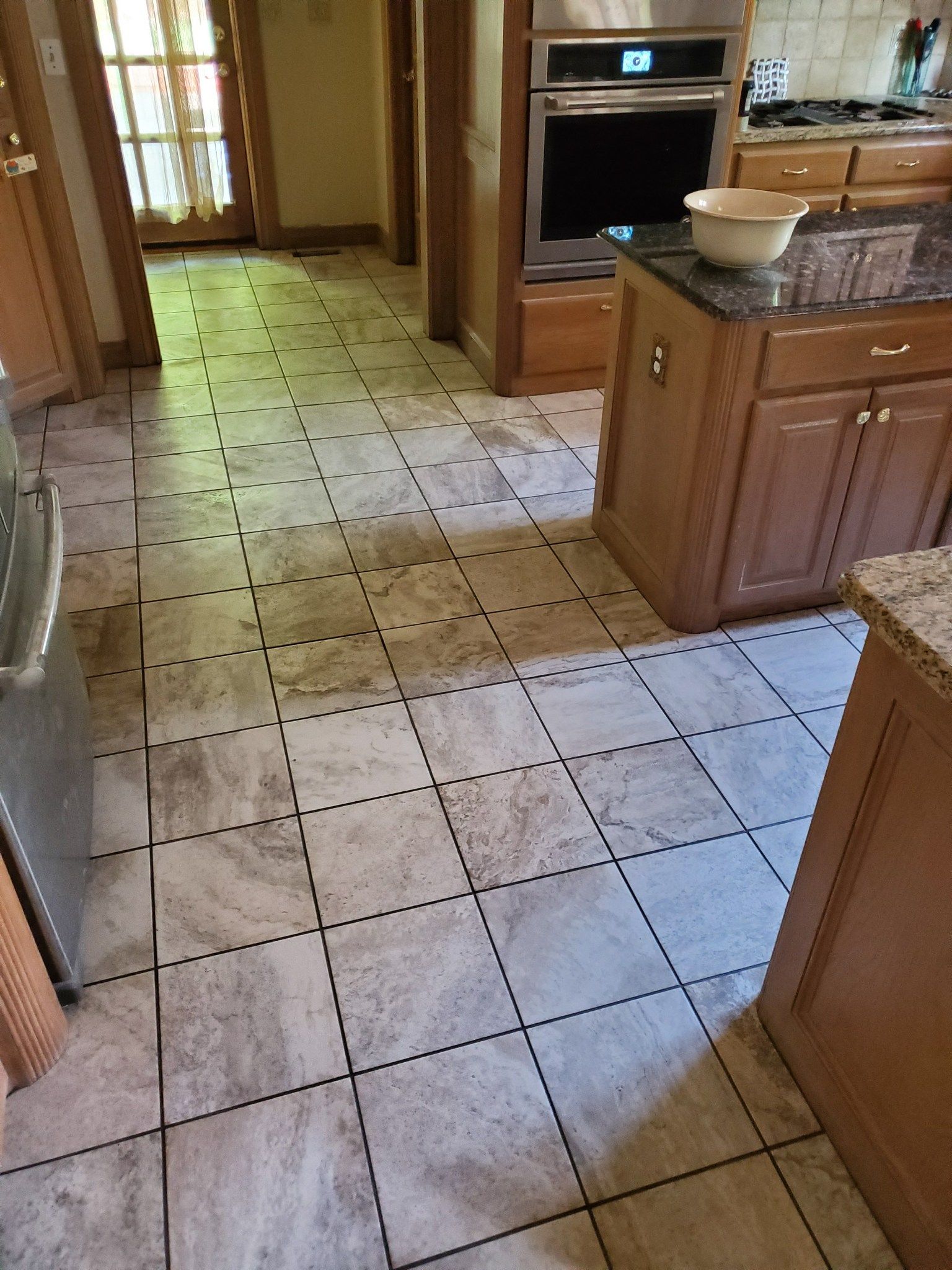 Kitchen with beige tile floor, wooden cabinets, granite island, and built-in oven in the background