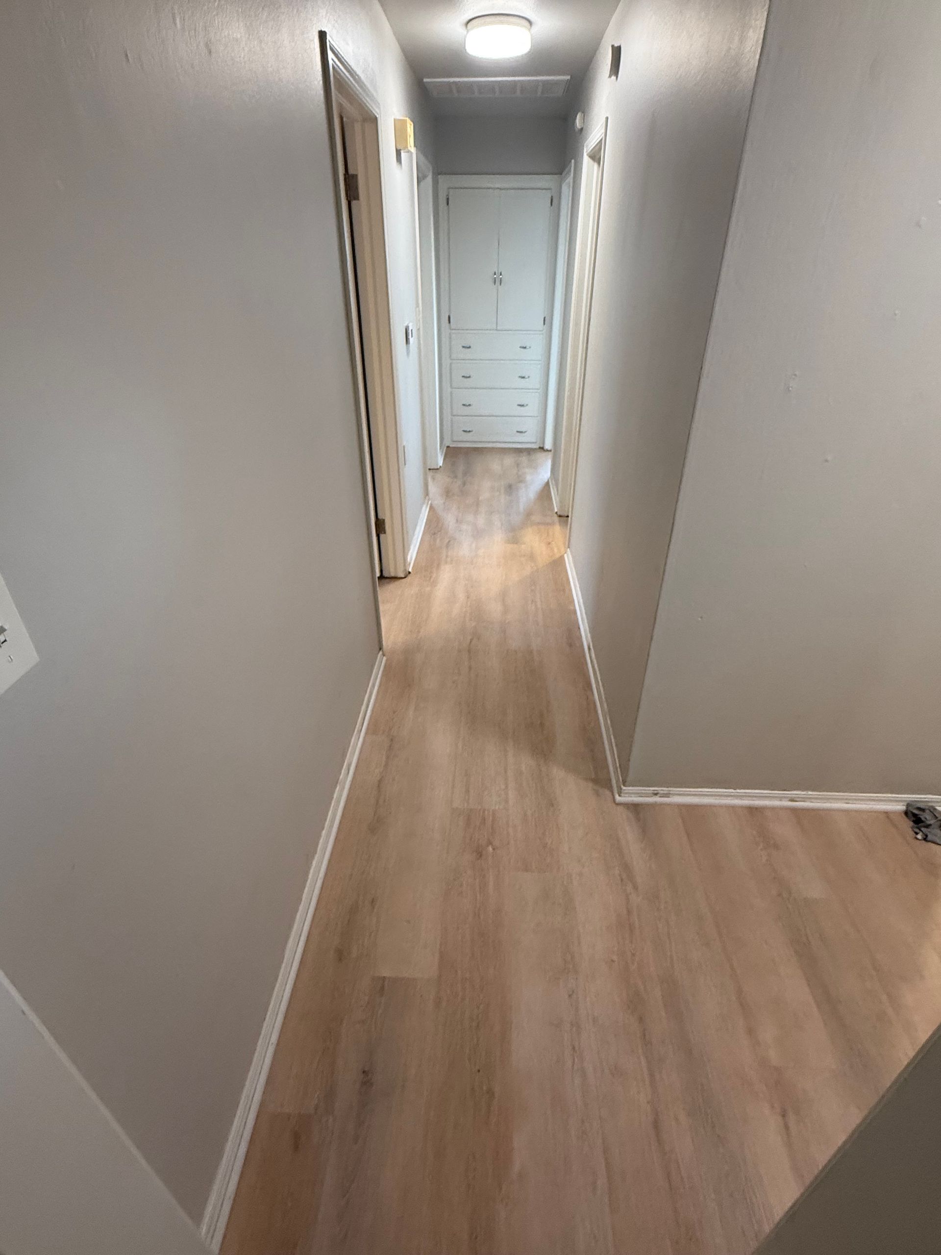 Narrow gray hallway with light wood floors and white doors at the end