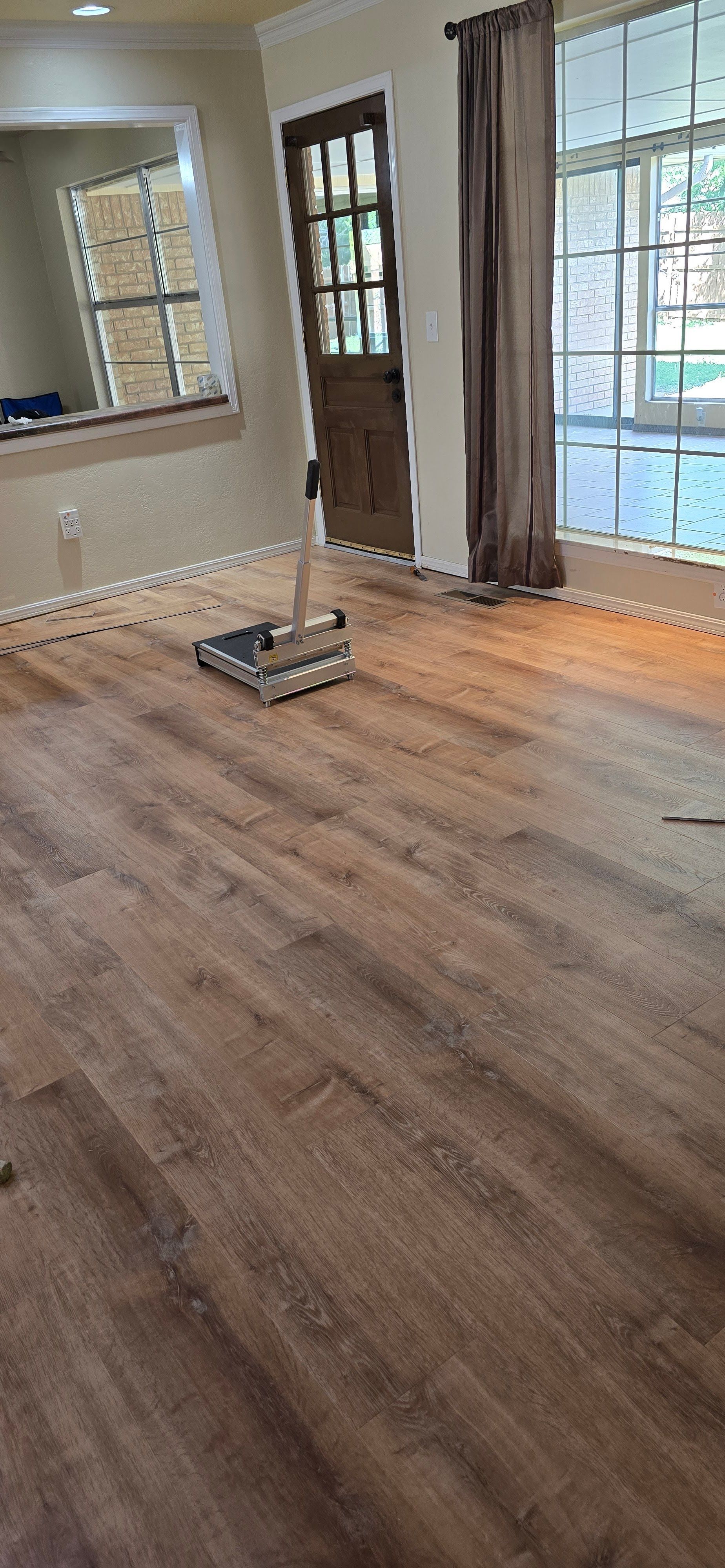 Empty hardwood living room with a small floor bracket near the center and windows with curtains.