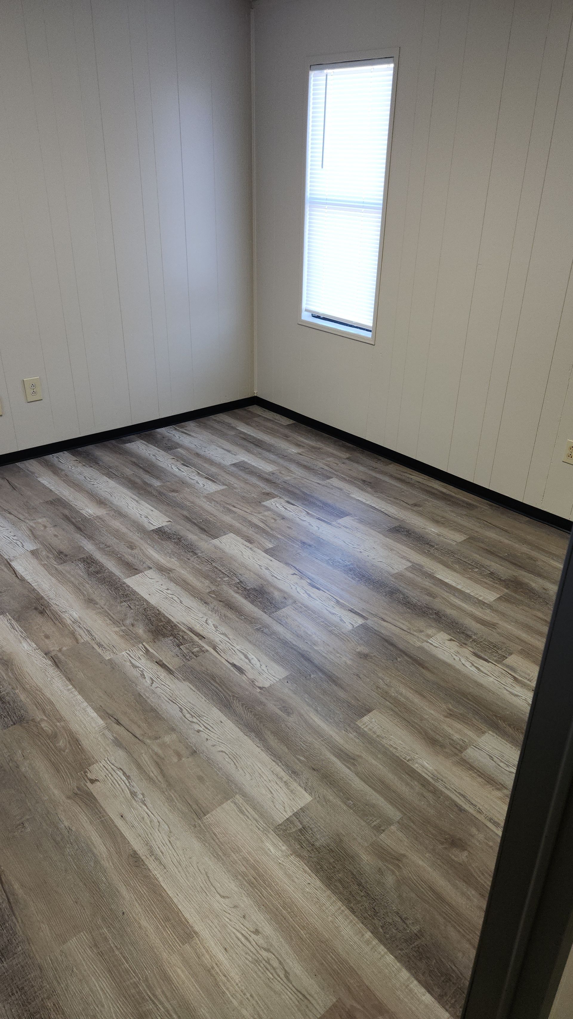 Empty room with wood-look flooring, off-white walls, and a single window.