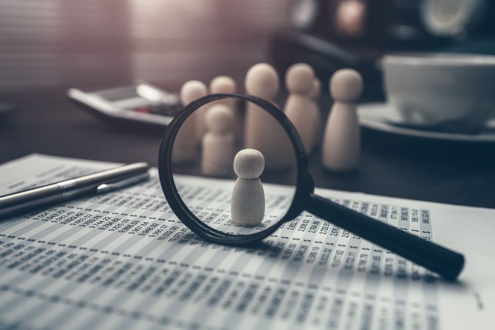 Magnifying glass over a row of small figures on paperwork, suggesting search or selection.