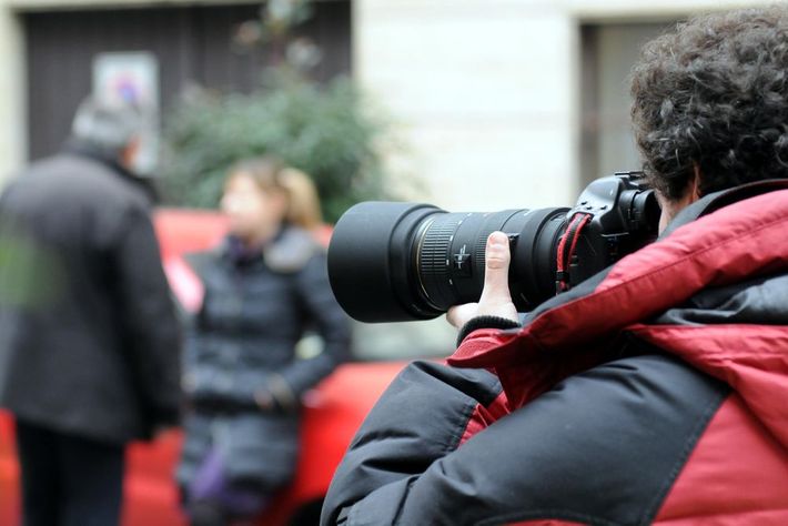 Photographer in a red jacket aiming a large camera at a blurred outdoor scene