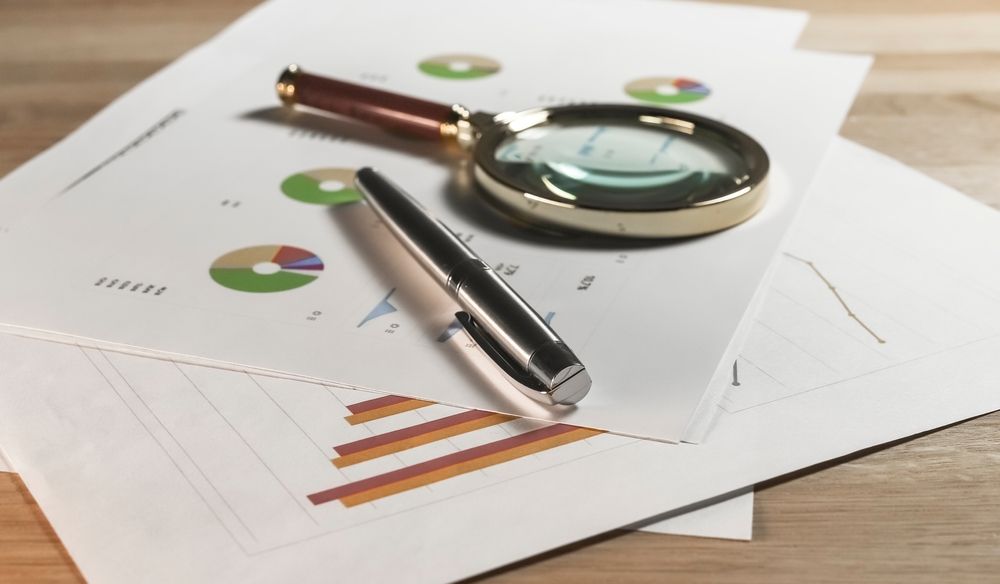 Magnifying glass and pen resting on business charts and graphs on a desk