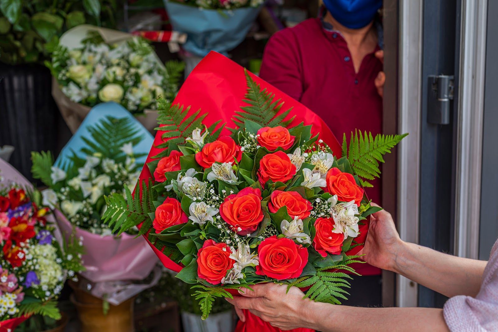 Hands holding a bouquet of red roses and white flowers at a flower shop counter