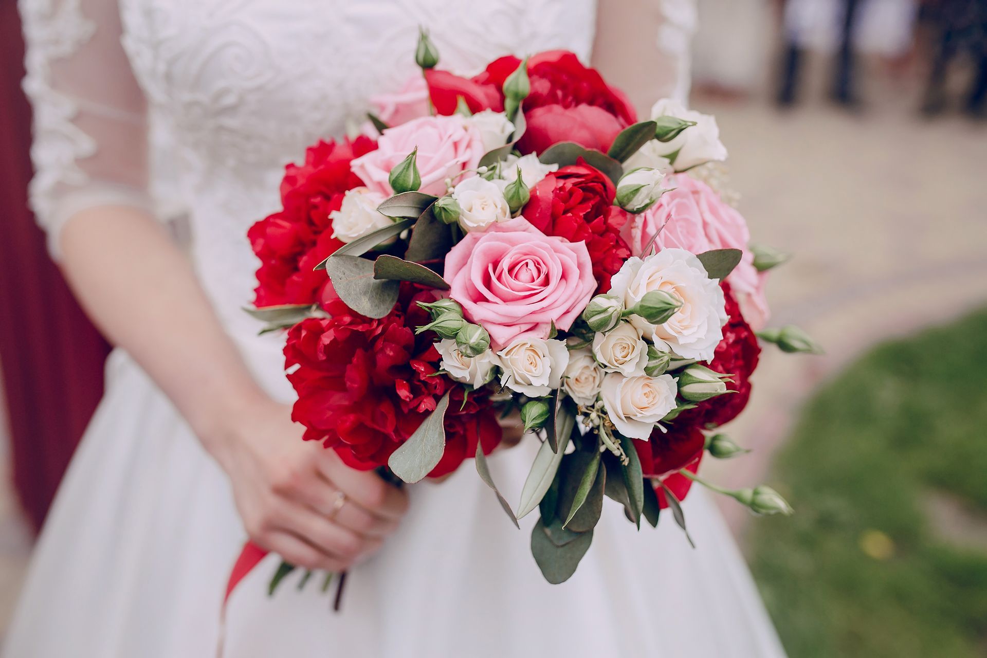 Bride holding a bouquet of pink and red flowers in a white dress