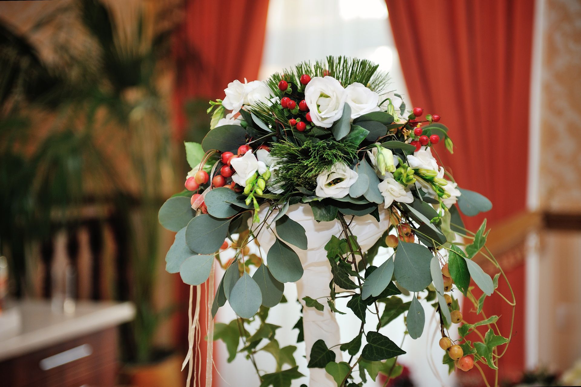 White floral arrangement with greenery and trailing vines on a decorated stand