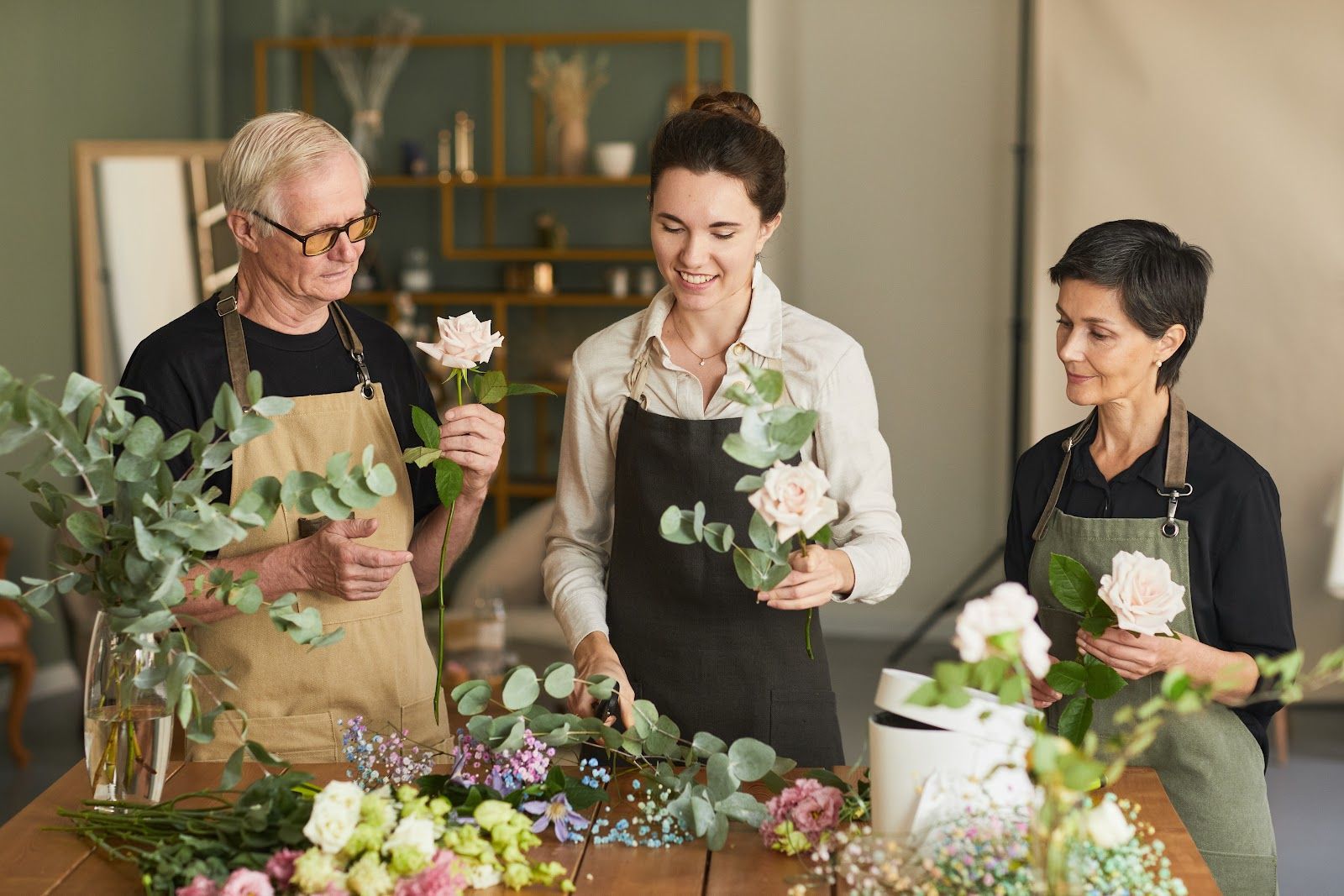 Three people arranging flowers at a table in a bright workshop