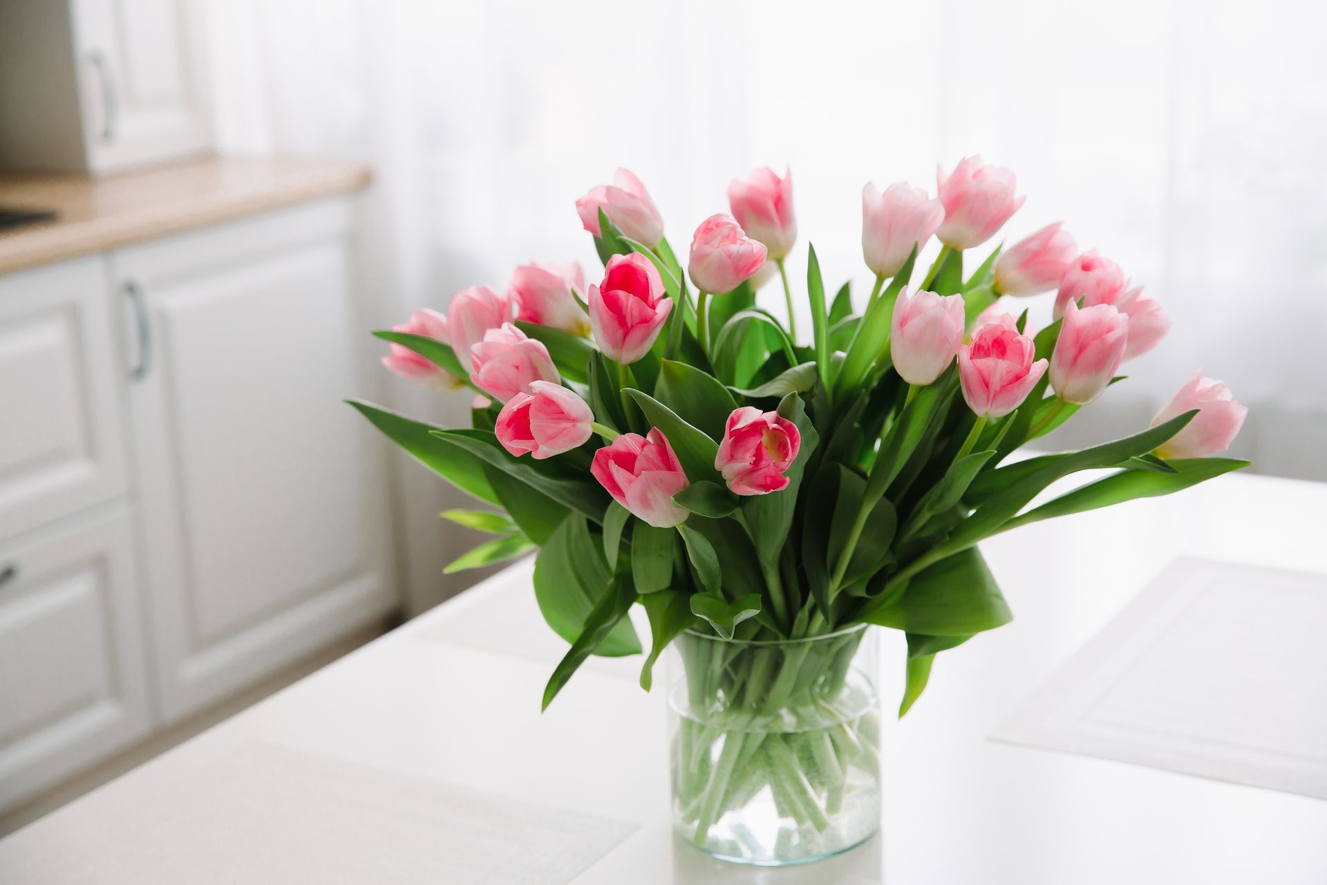 Bouquet of pink tulips in a glass vase on a bright kitchen table