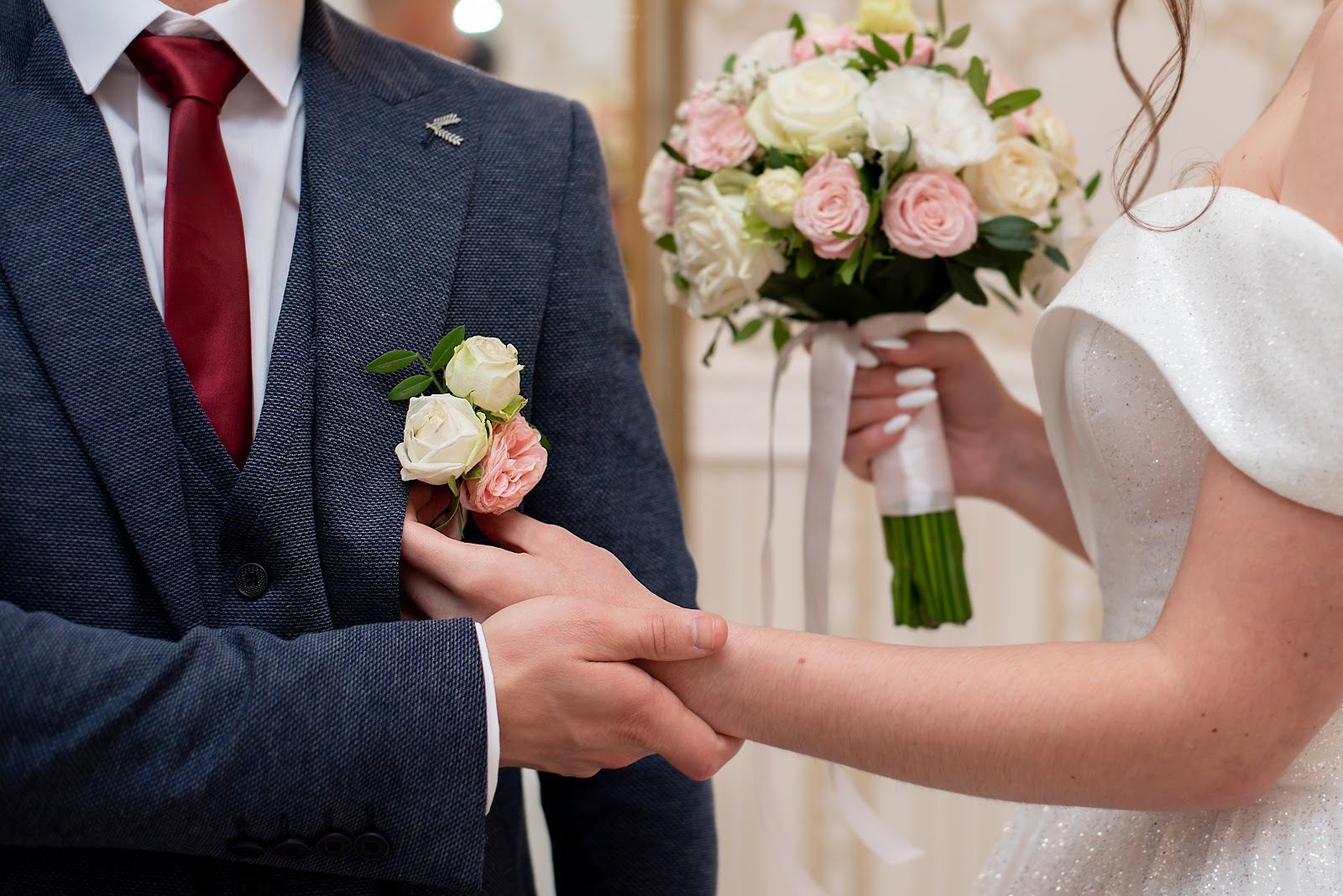 Bride and groom holding hands during a wedding ceremony, with bouquet and red tie visible