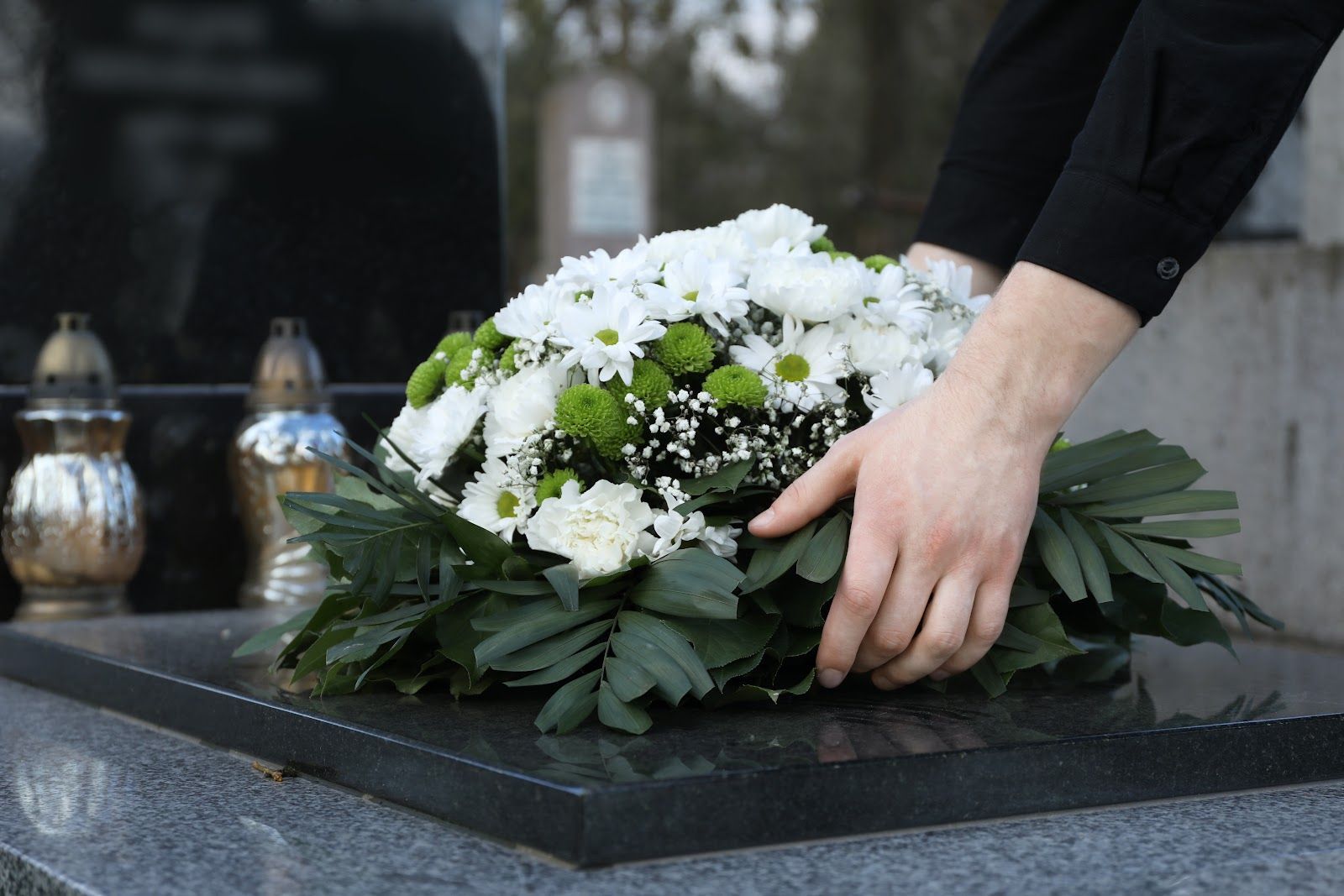 White floral wreath being placed on a gravestone at a cemetery, with hands arranging it.