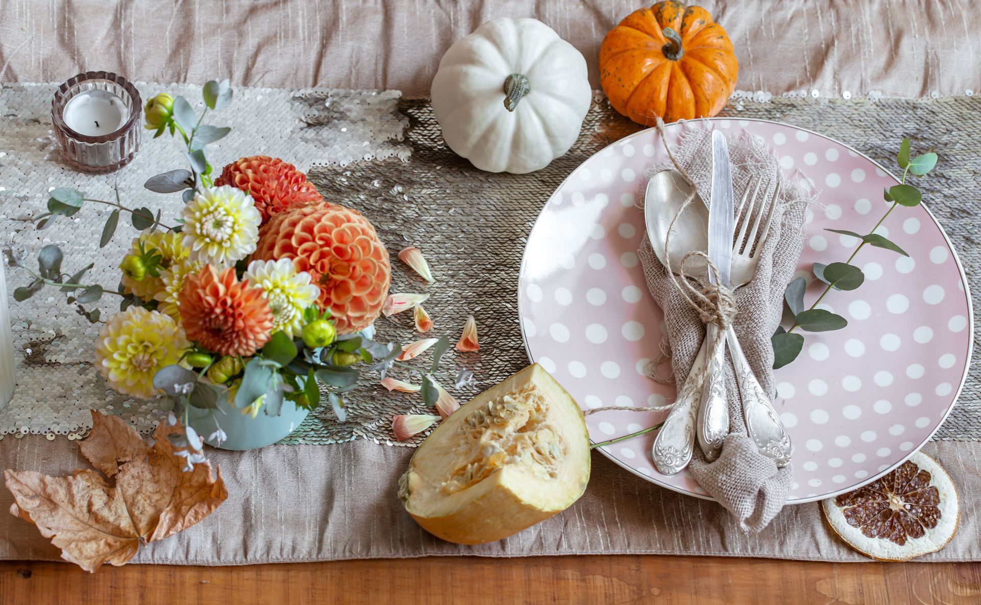 Fall table setting with flowers, pumpkins, a pink polka-dot plate, and napkin on rustic wood.