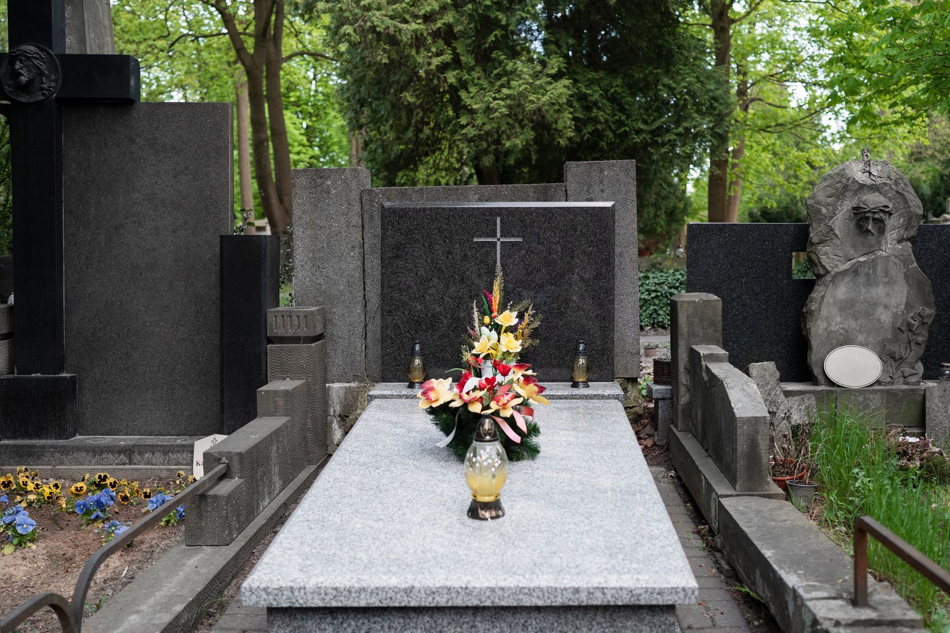 Gravestone with flowers in a cemetery, framed by trees and surrounding headstones