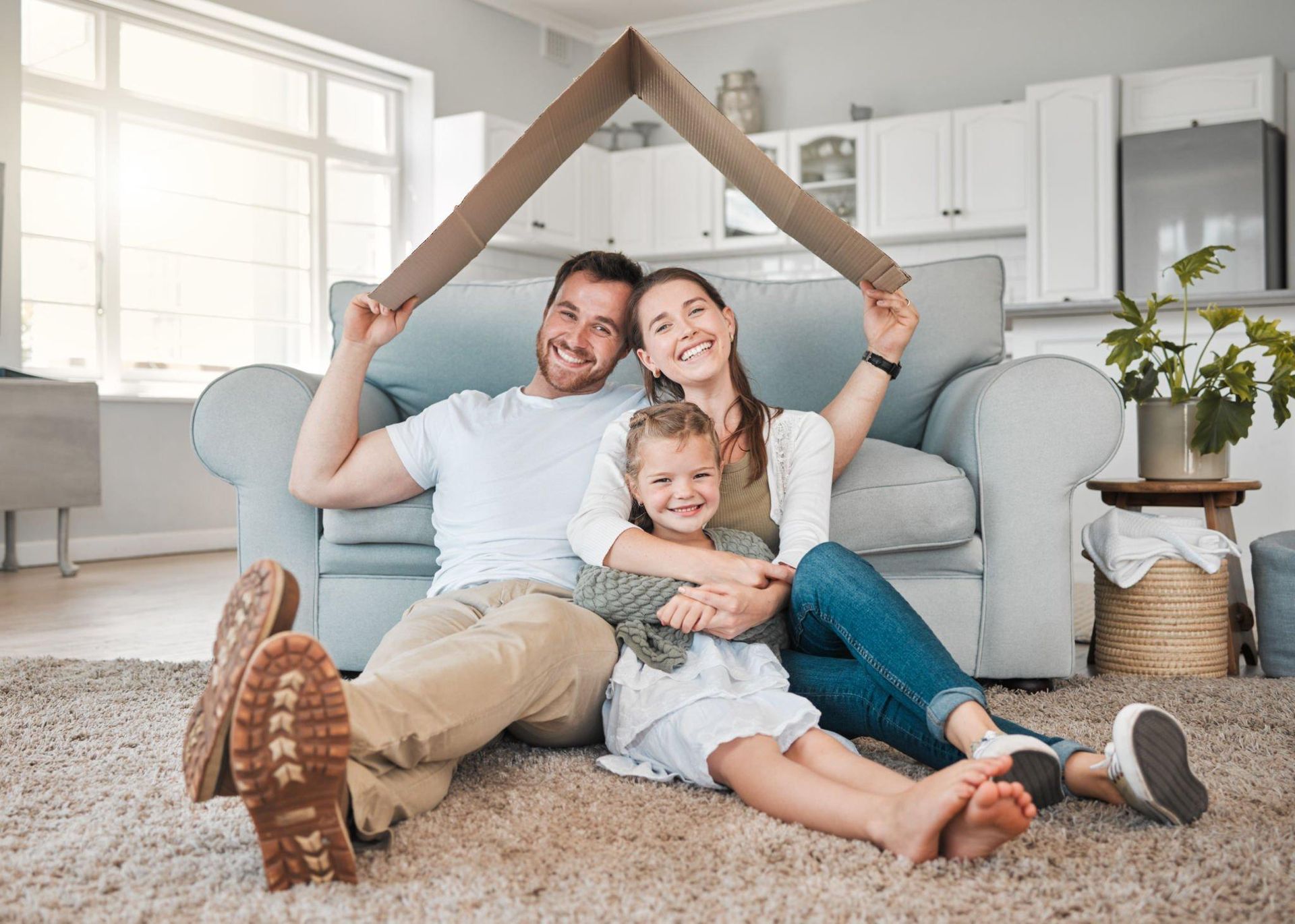 A family is sitting on the floor under a cardboard house.