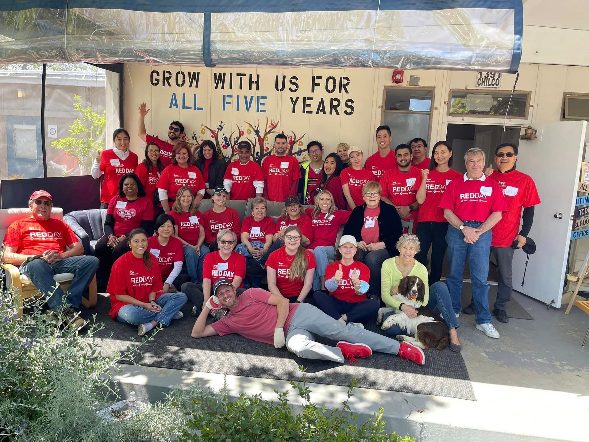 A group of people are posing for a picture in front of a sign that says `` grow with us for all five years ''.