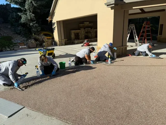 workers hand-troweling a brown rubber coating onto a patio driveway