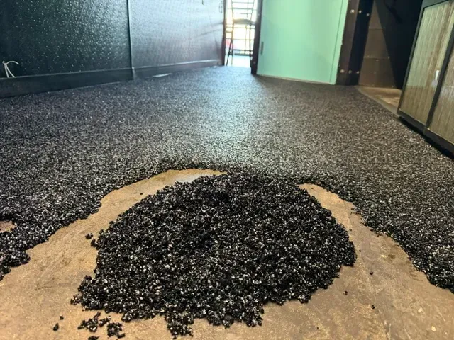 Pile of black rubber safety granules being poured and spread onto a concrete floor