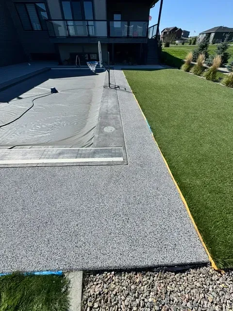 A freshly resurfaced speckled gray rubber safety coating on a pool deck