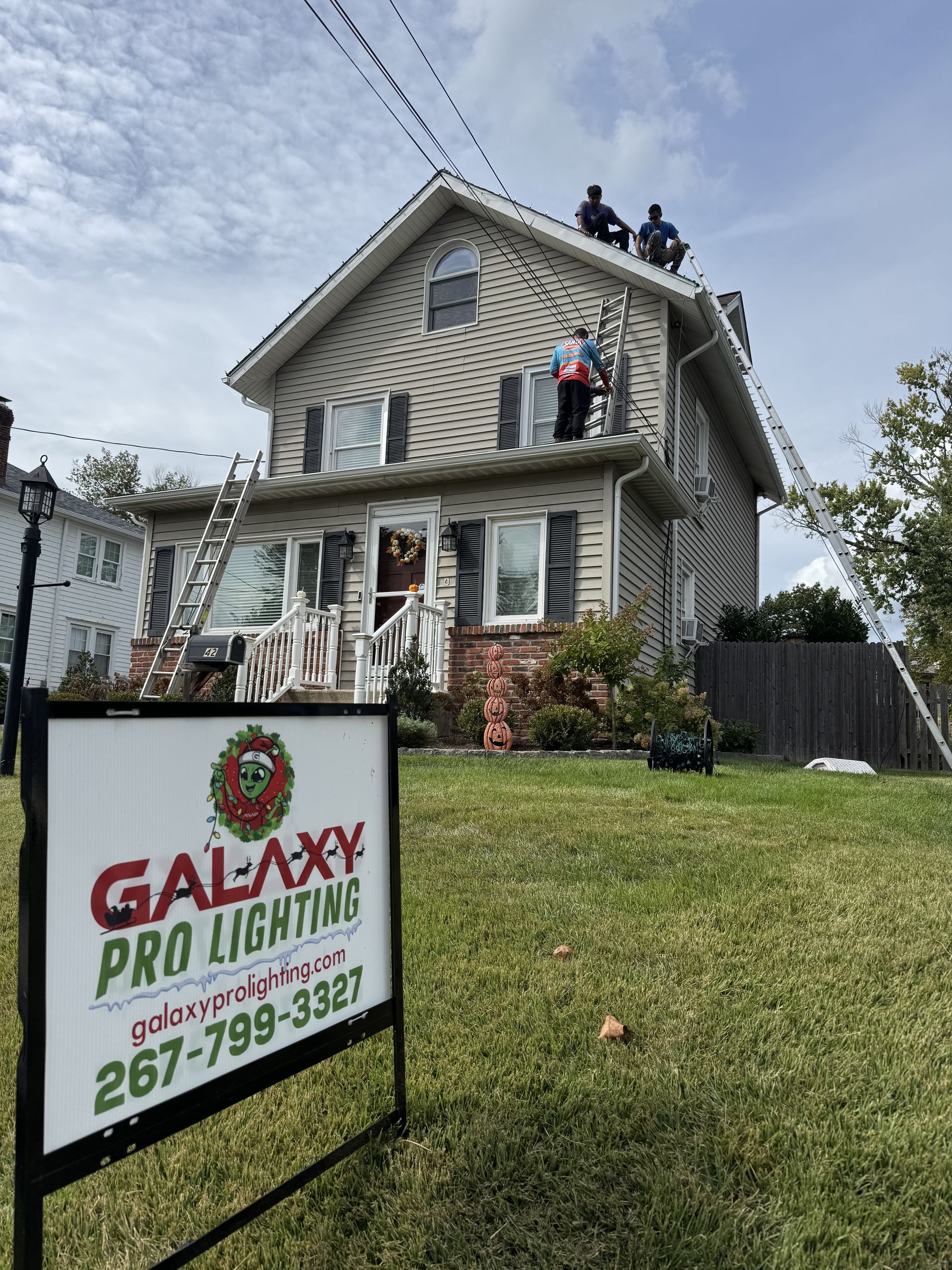 Two men on a roof installing lights on a two-story beige house. 