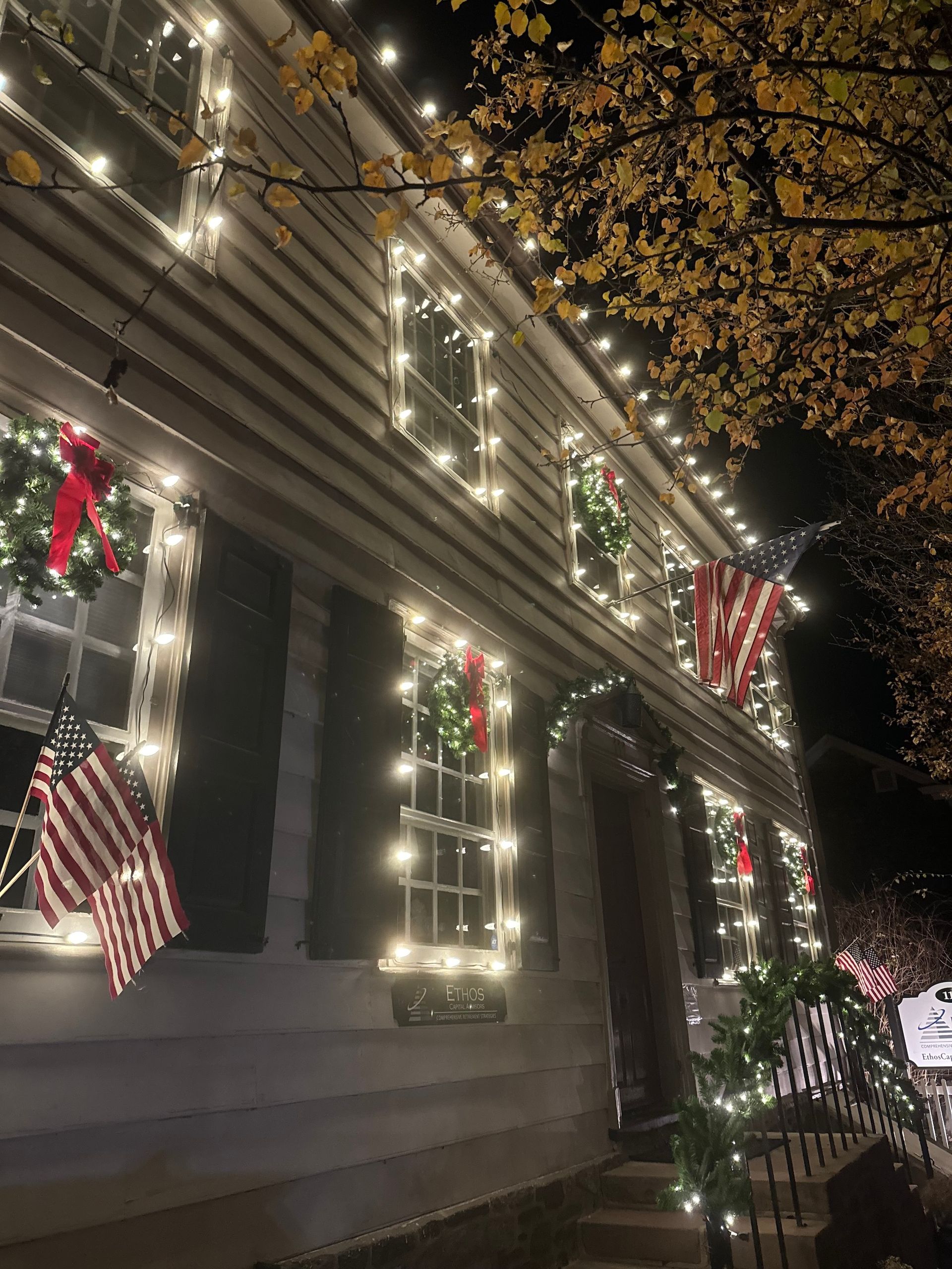 A two-story house with Christmas lights, wreaths, and American flags at night.