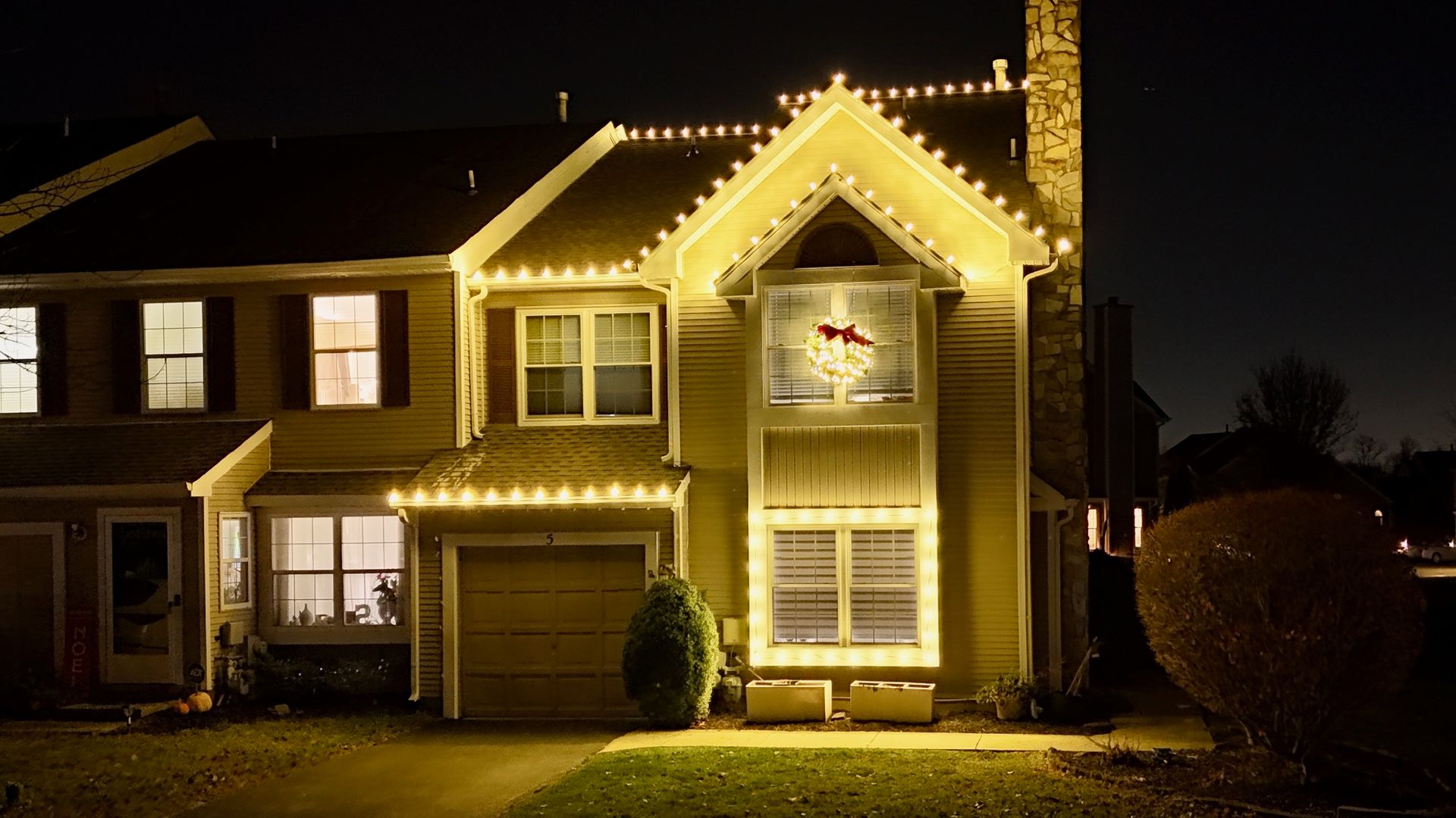 House at night with yellow Christmas lights outlining roof and windows.