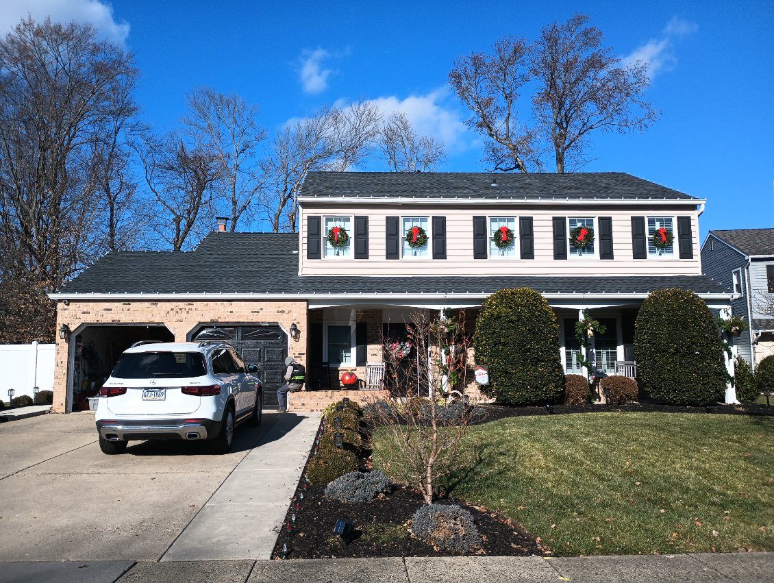Two-story house with wreaths on windows; white SUV in driveway; clear blue sky.