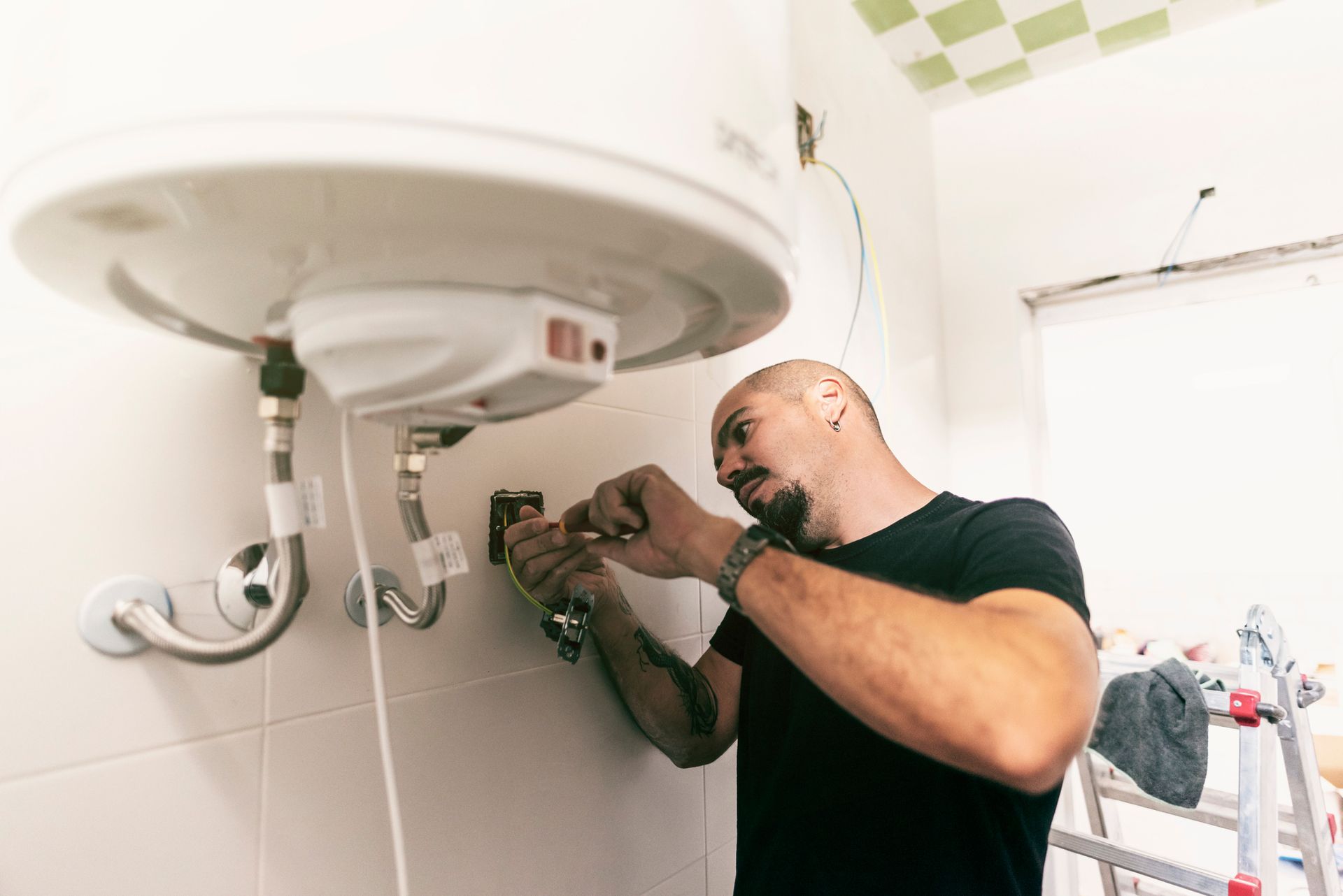 A man is fixing a water heater in a bathroom.