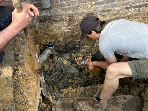 Two men are working on a pipe in a hole in the ground.