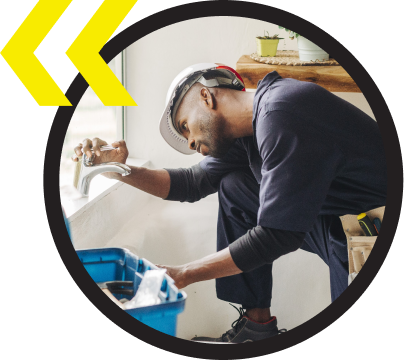 A man wearing a hard hat is working on a sink A man wearing a hard hat is working on a sink