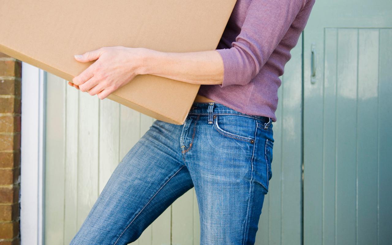 Person carrying a large cardboard box near a doorway
