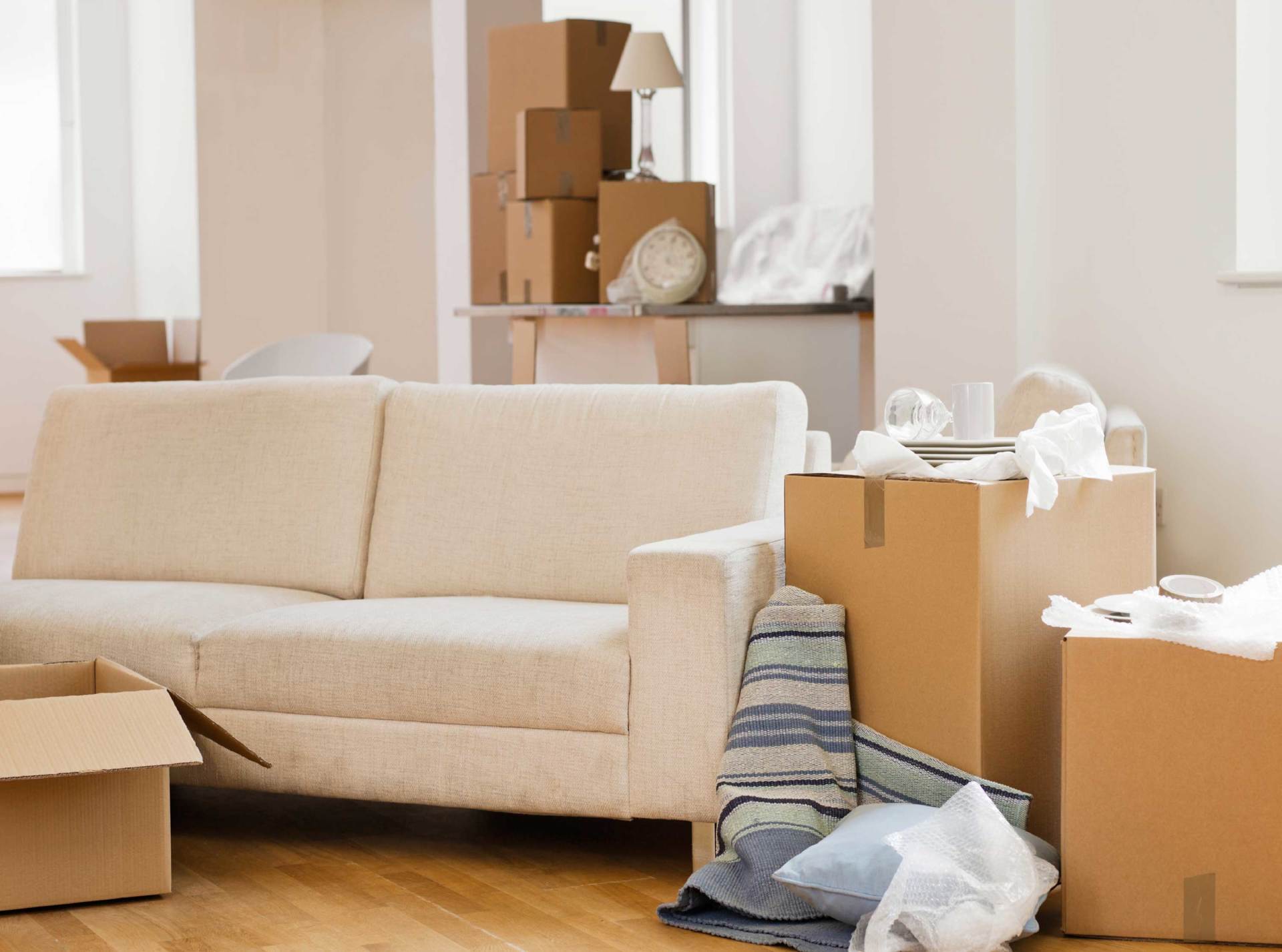Unpacked living room with beige sofa, moving boxes, and scattered packing materials
