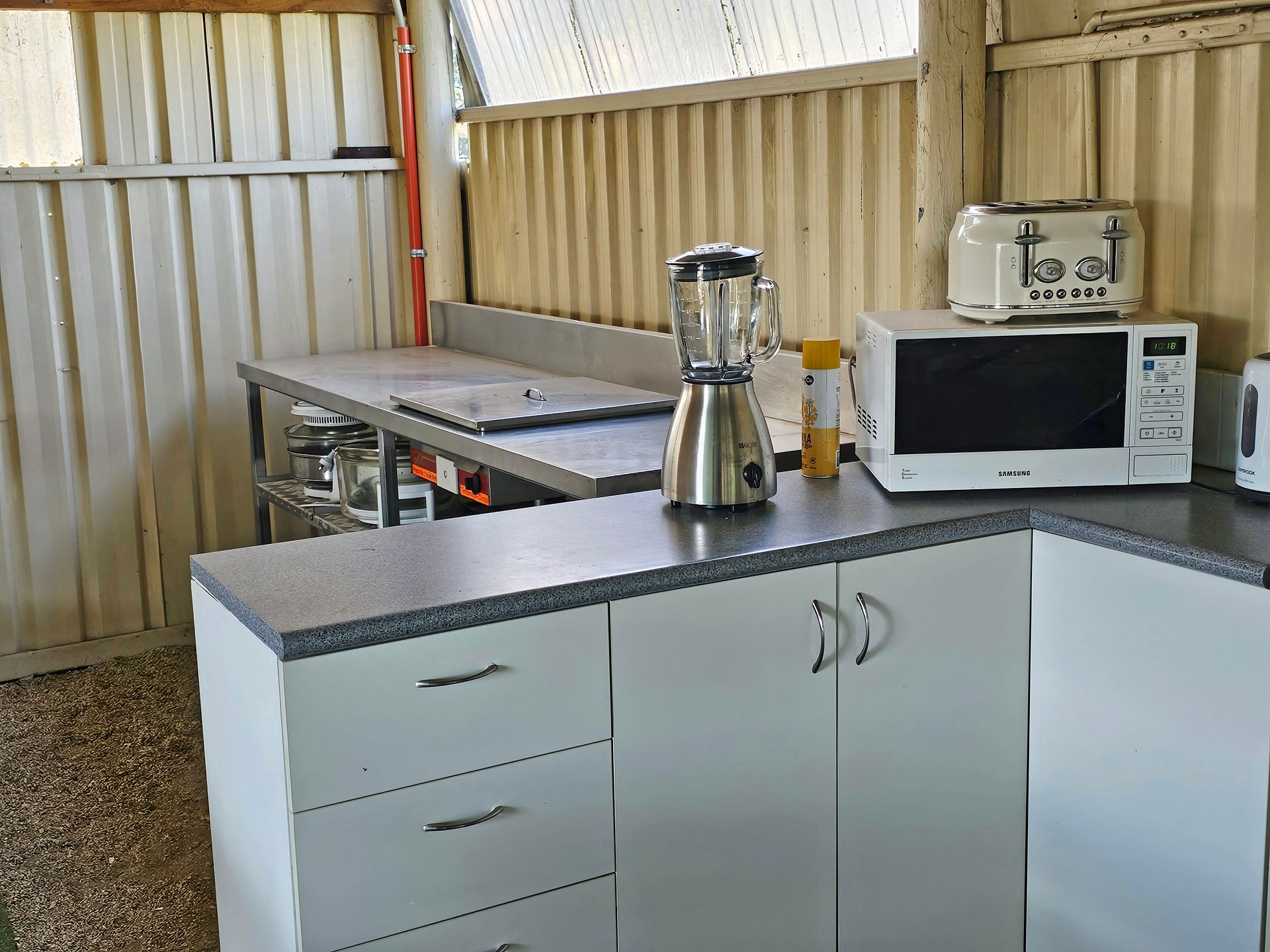 Small kitchen area with white cabinets, a countertop blender, and a microwave against corrugated metal walls.