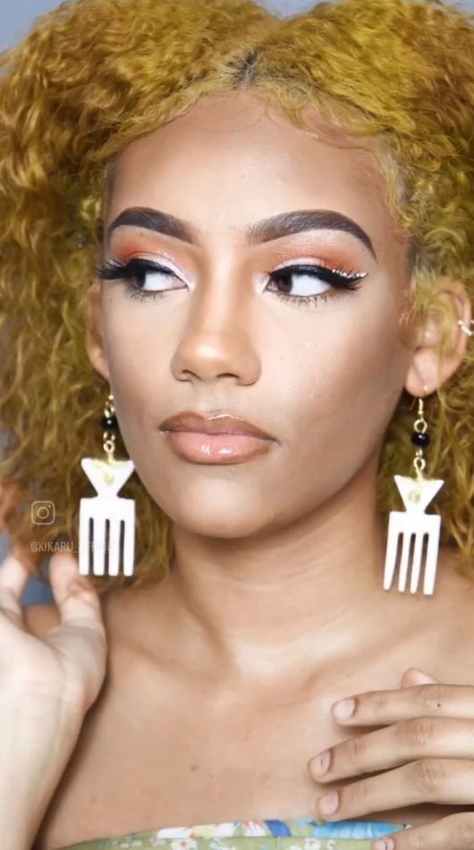 Woman with golden hair wearing white and black geometric earrings, makeup, and looking to the side.