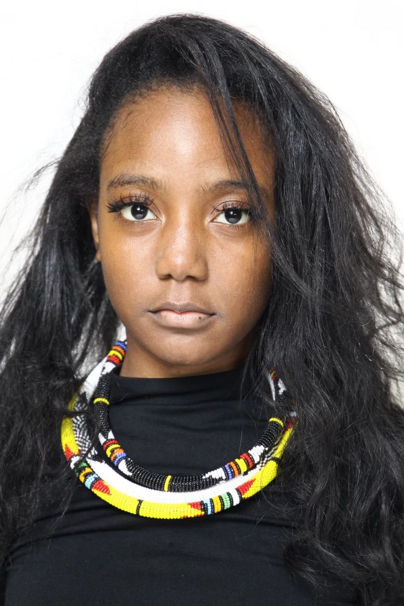 Woman with long black hair, wearing a colorful beaded necklace and black top.