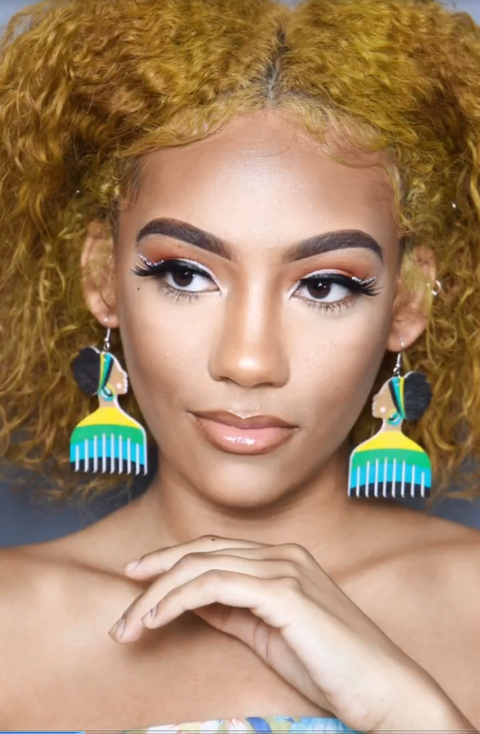 Woman with golden hair wearing colorful afro-pick earrings, looking left, off-shoulder top.