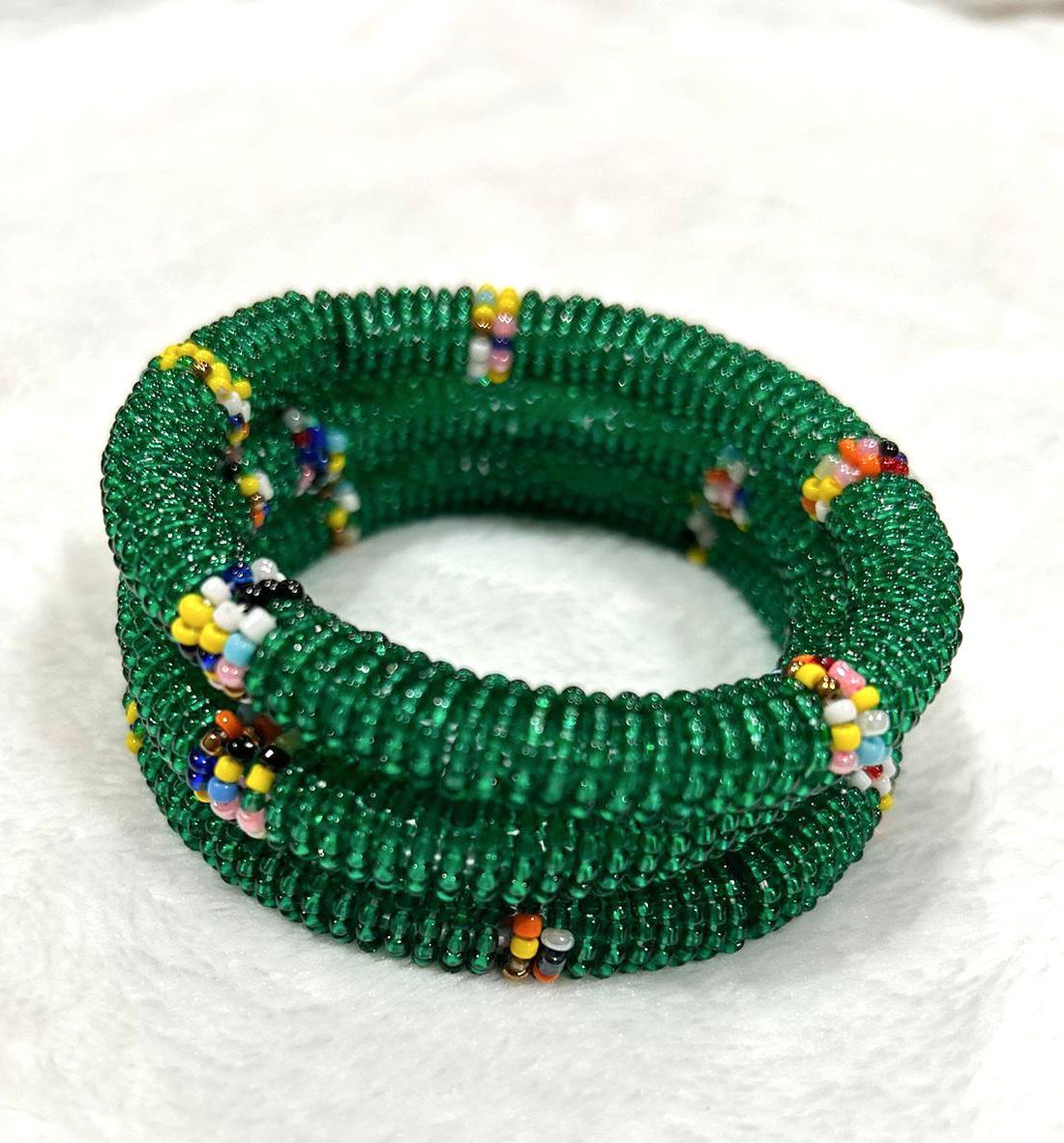 Green beaded bracelet coiled on a white surface, with colorful accent beads.