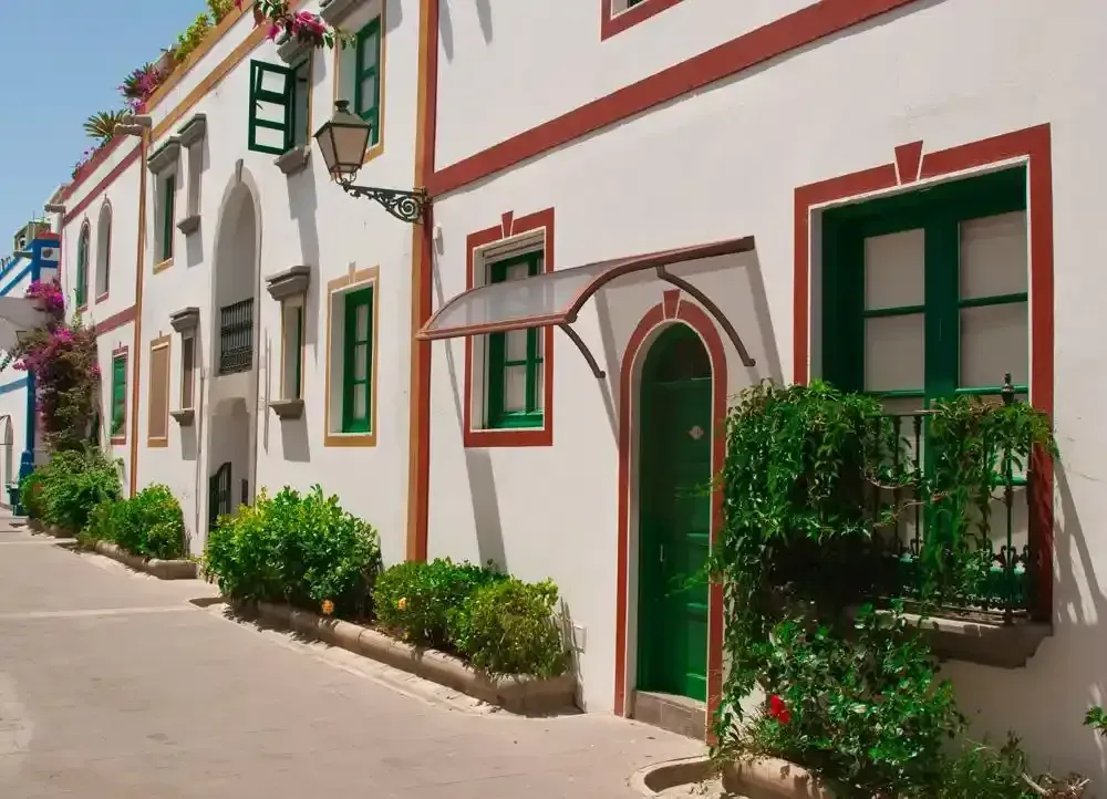 Viale bianco di paese con porte e finestre ad arco colorate e piante in vaso in una giornata di sole