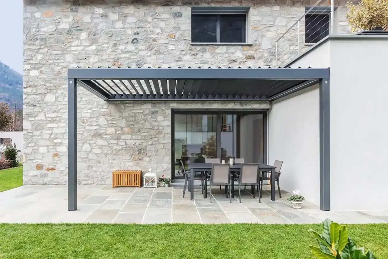 Patio in pietra con pergola grigia e tavolo da pranzo all'aperto accanto a una casa moderna.