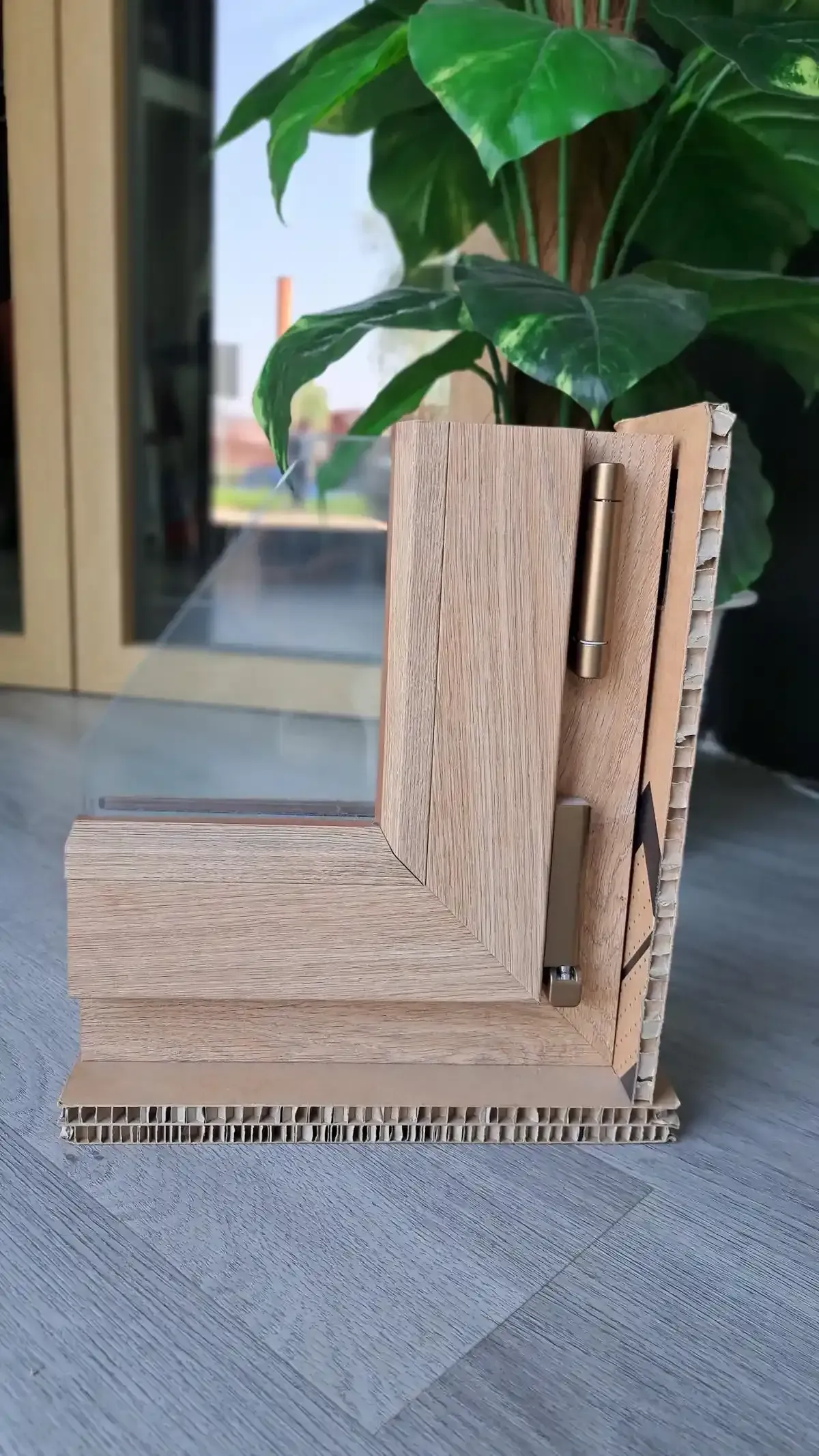 Prototipo di giunto a cerniera a L in legno per piano di tavolo, accanto a una pianta verde in interni.