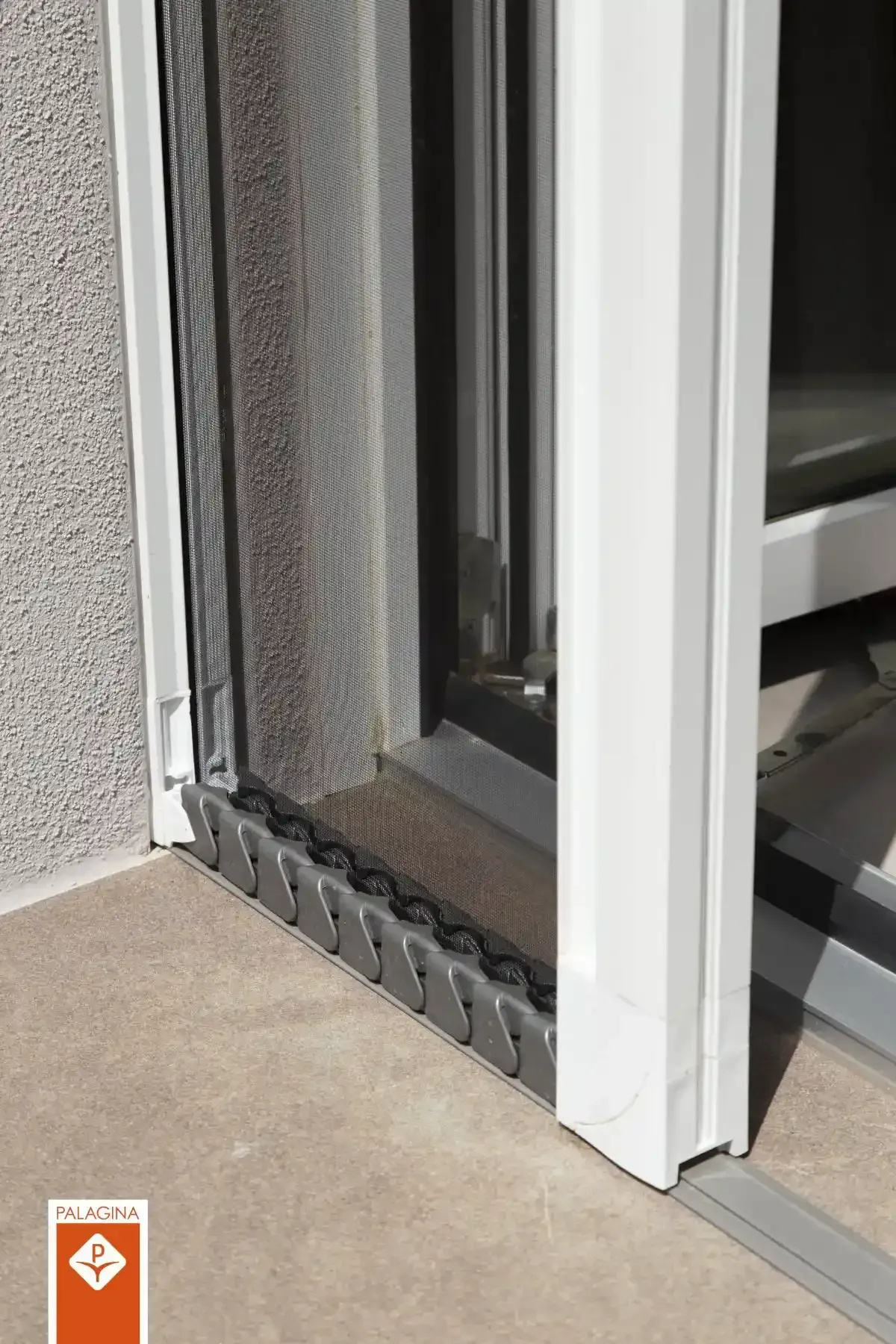 Primo piano della soglia di una porta scorrevole in vetro con fermaporta nero e pavimento in cemento del patio.