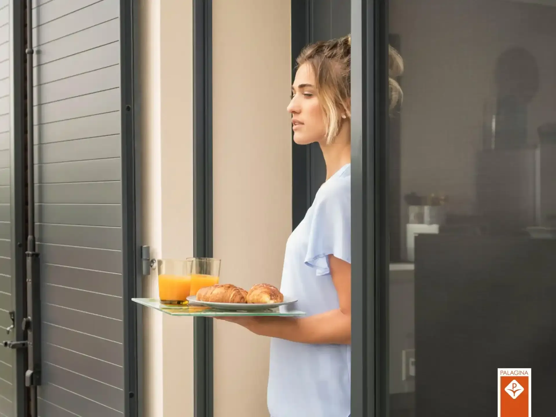 Una donna porta un vassoio con cibo e bevande attraverso la porta di un appartamento moderno.