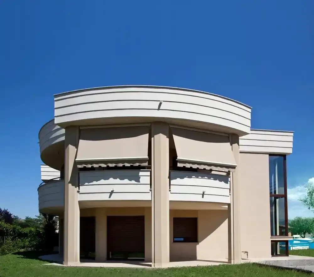 Casa moderna beige a due piani con balcone curvo e finestre tinte di blu sotto un cielo limpido