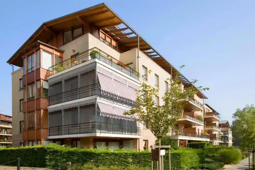 Moderno condominio con balconi, dettagli in legno e vegetazione lungo una strada