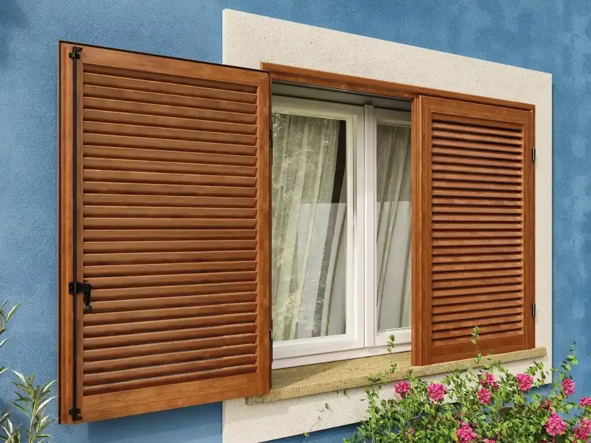 Persiane in legno incorniciano una finestra su una parete di stucco blu con fiori sottostanti.