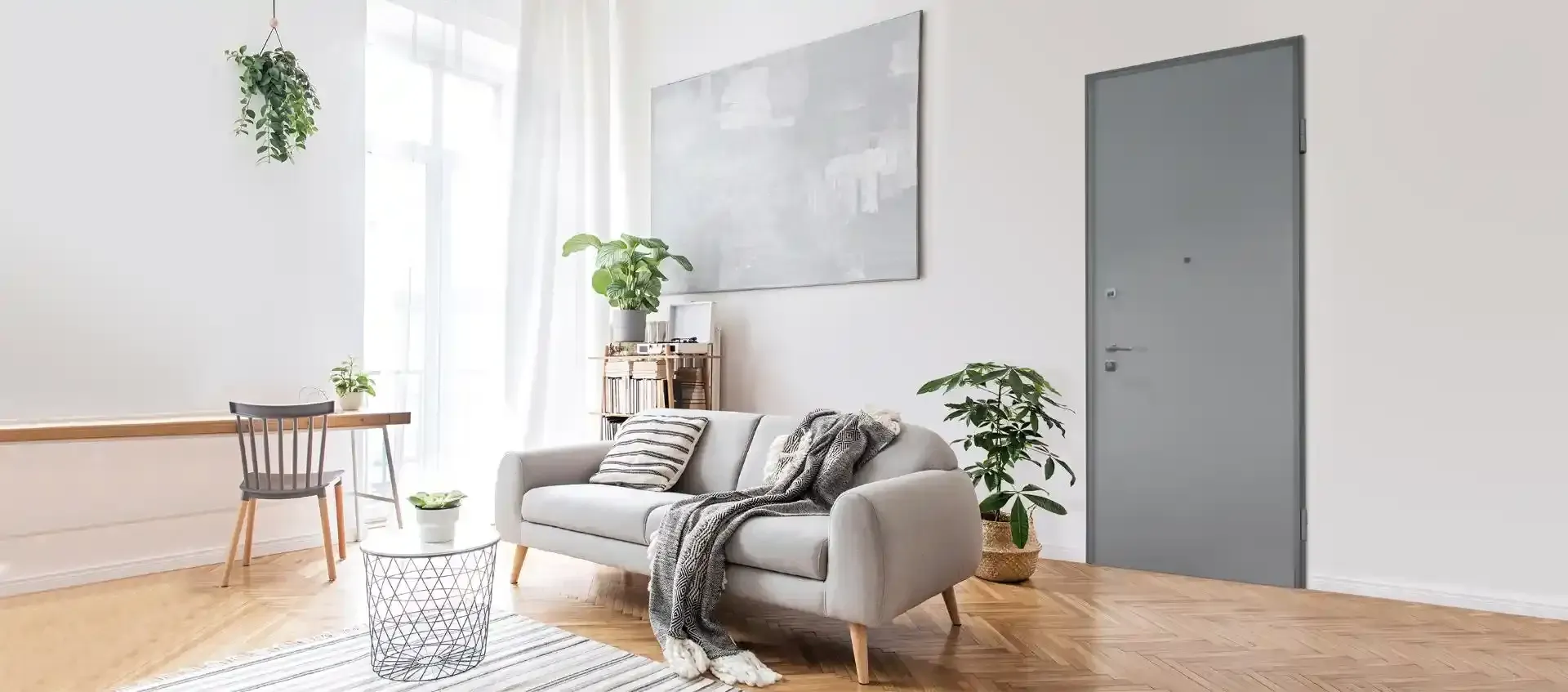 Luminoso soggiorno minimalista con divano grigio, piante, pavimento in legno e pareti bianche.
