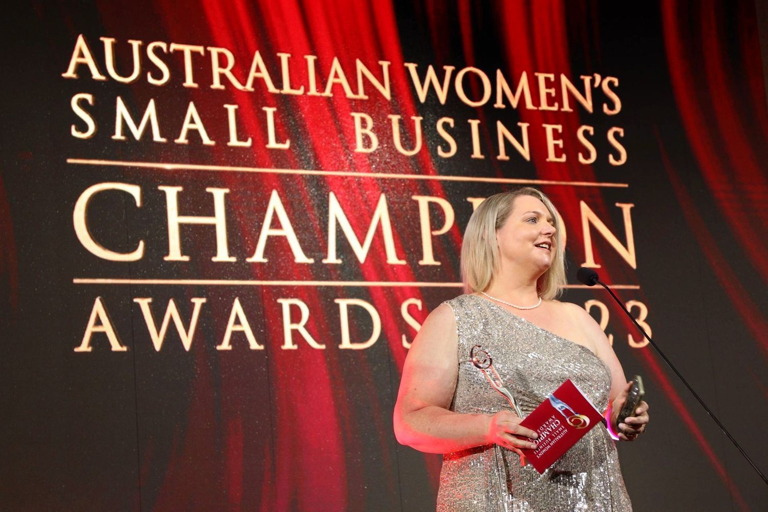 A woman is standing in front of a sign that says australian women 's small business champion awards