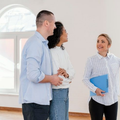 Three people in a bright room discussing a wall of windows, one gesturing while holding a blue folder