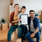 Family on a couch holding a sign that says “Our First Home”